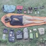 un homme allongé sur un sac de couchage dans l'herbe entouré d'équipements de rando