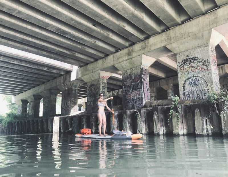 une femme passe en paddle sur une rivière sous un pont