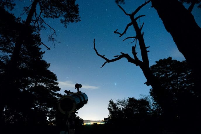 un télescope en forêt pointé vers le ciel étoilé